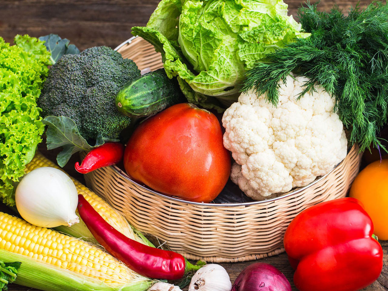Vegetable basket full of cauliflower, lettuce, broccoli, red peppers, garlic, corn chilies, and tomatoes